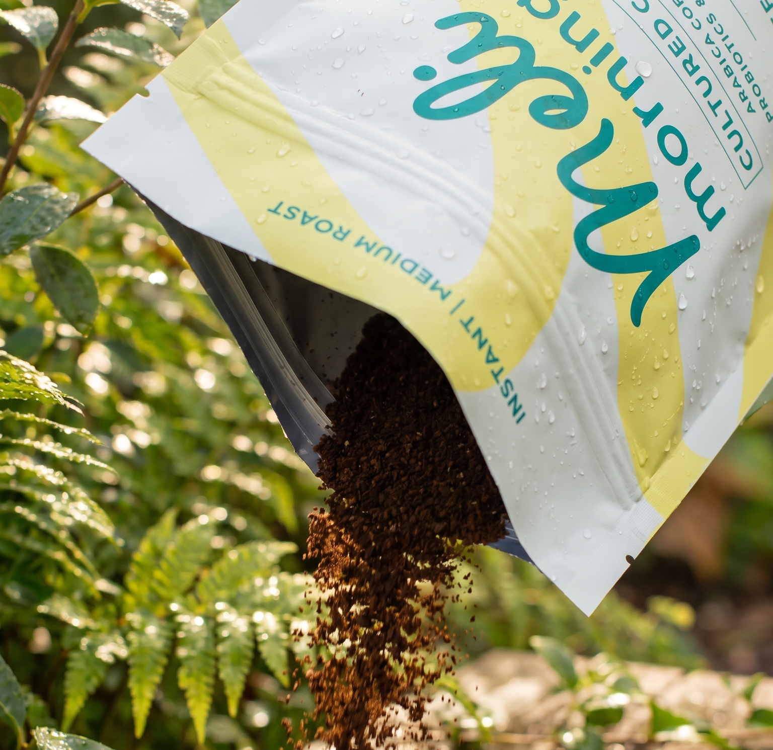 Meli Mornings Cultured Coffee pouch pouring instant coffee beside tropical greenery.